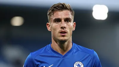 A mid-30s anonymous Lillestrøm SK midfielder in a solid blue kit, head-and-shoulders shot, focused expression, stadium...