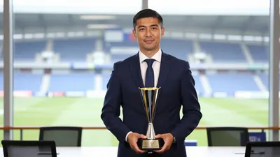 A 35-year-old male sporting director in a dark blue suit, standing in a football club office, holding a trophy, with a...